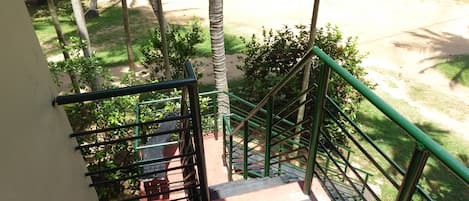 A staircase with green railings leading to a covered outdoor area with trees and a dirt path.