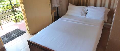 A single bed with white linens in a room with a tiled floor and a door leading to an outdoor area with a metal railing.
