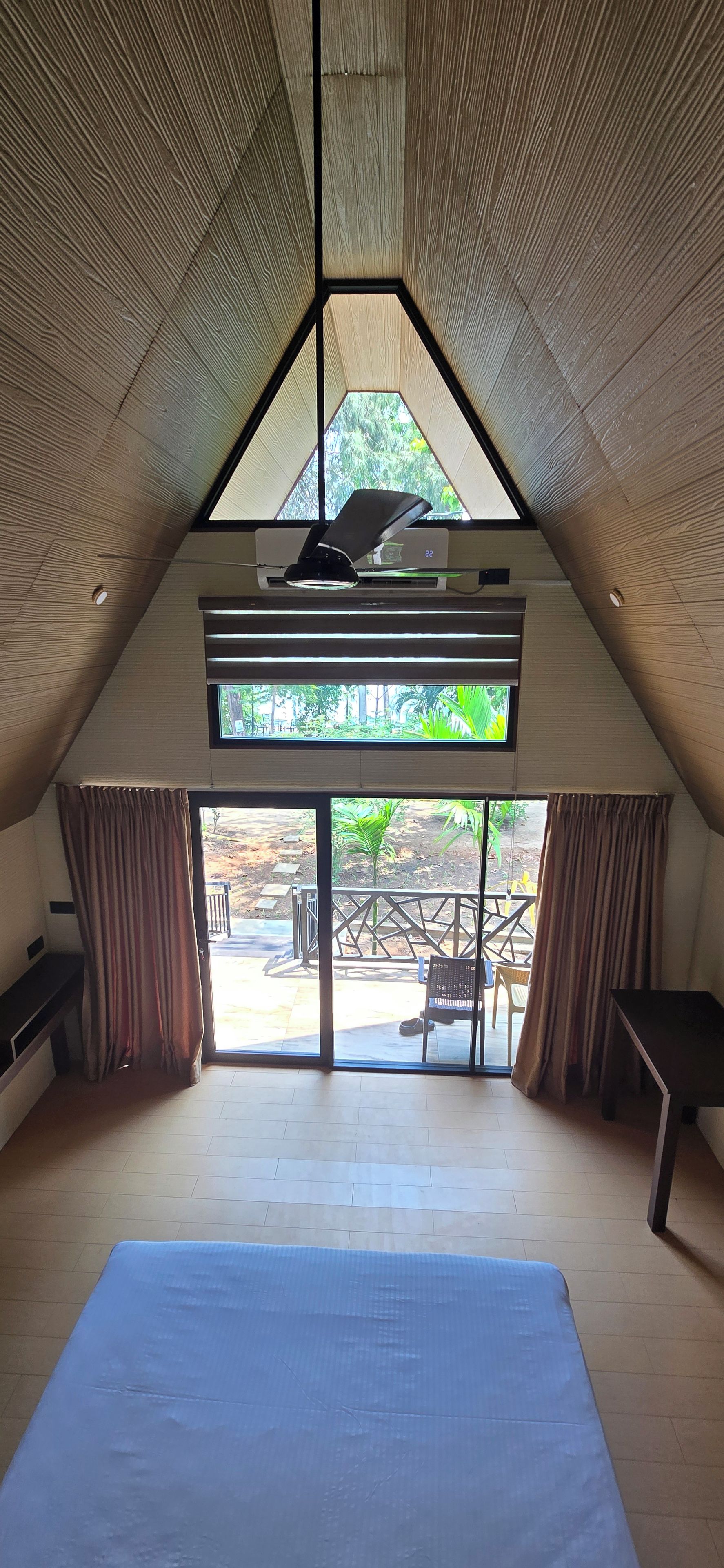 Una habitación con techo inclinado, una cama, un ventanal y vistas a un espacio exterior con mesa y sillas.