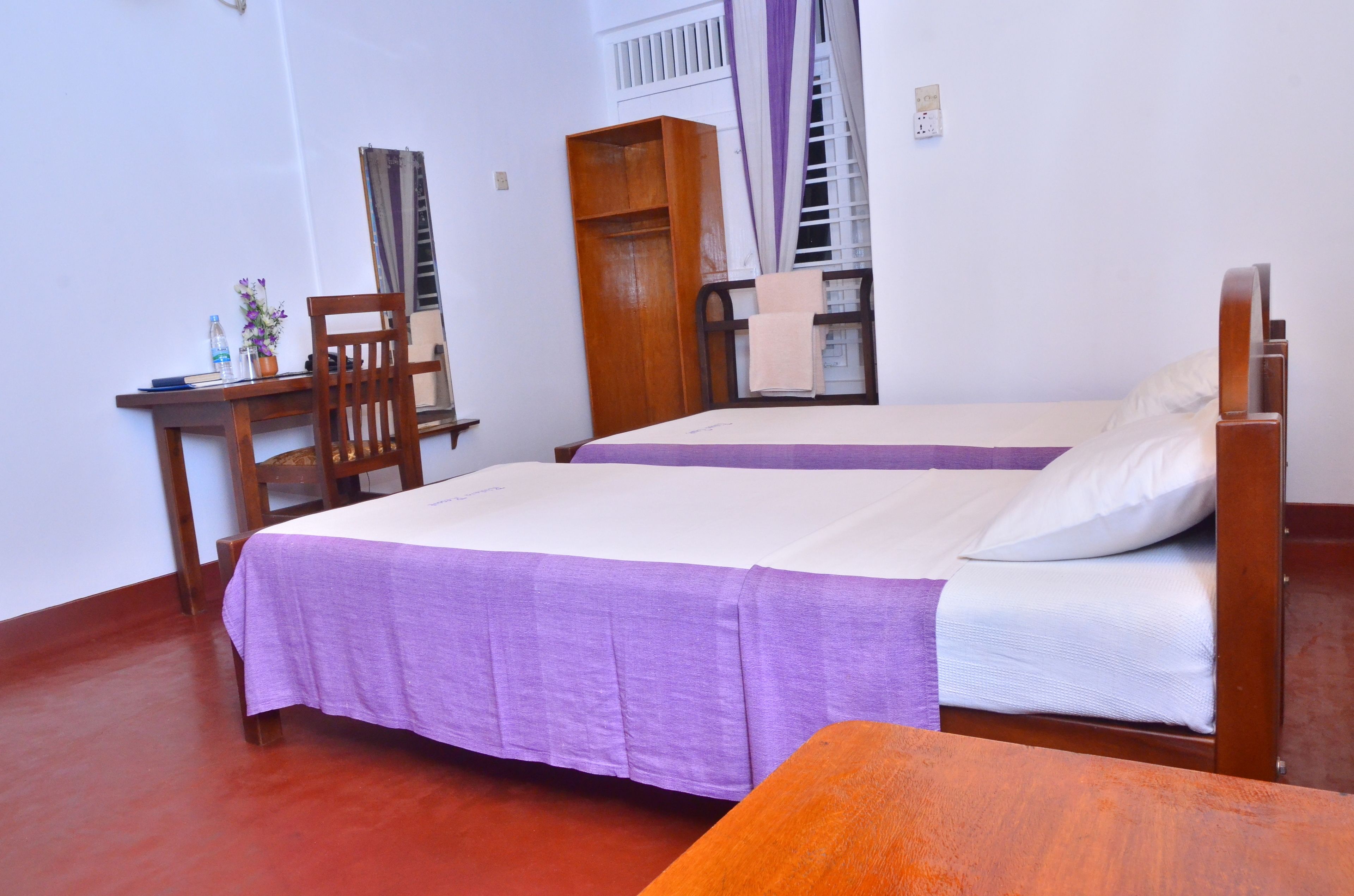 A room with two beds, a wooden desk, a chair, and a wardrobe.