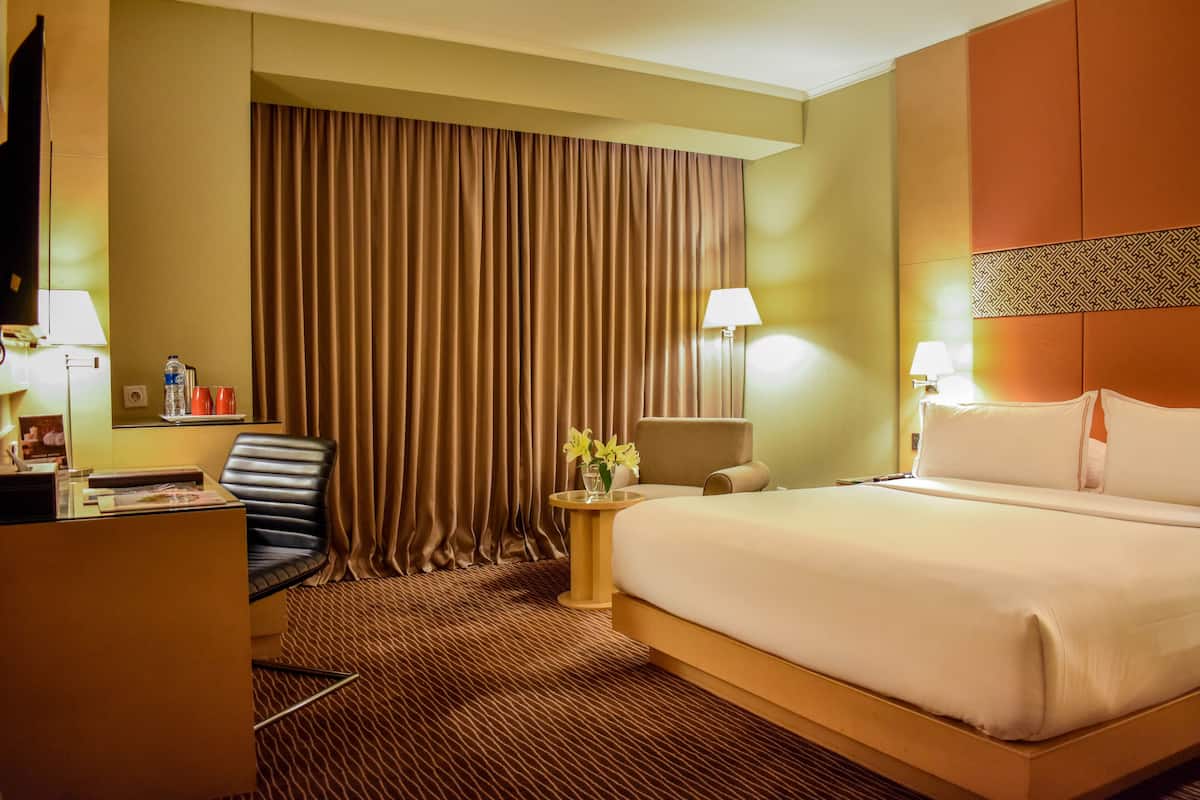 Ein Hotelzimmer mit einem großen Bett, einem Schreibtisch, einem Sessel, einem Nachttisch mit Lampen und einem Vorhang.