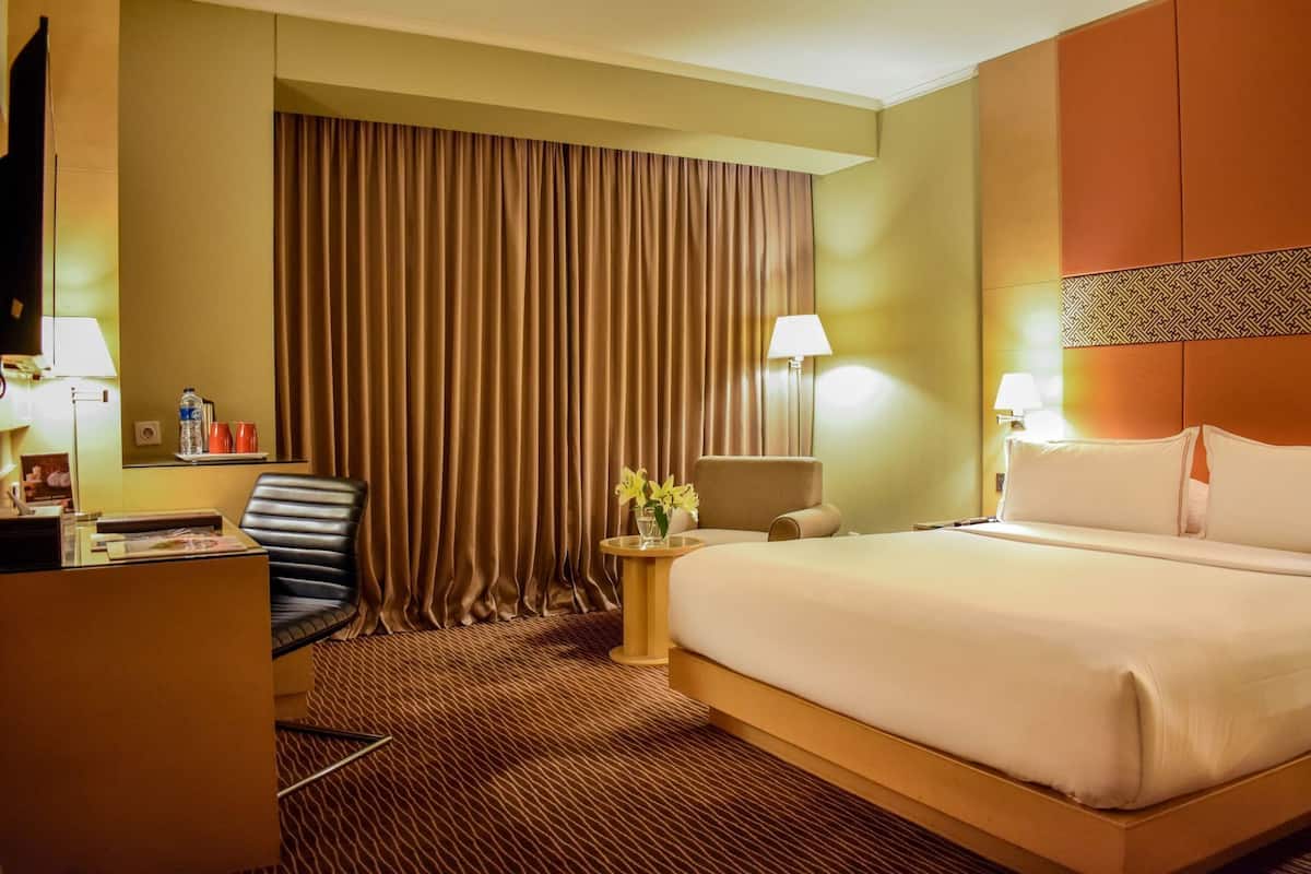 Ein Hotelzimmer mit Bett, Schreibtisch, Stuhl, Lampe und Vorhang.