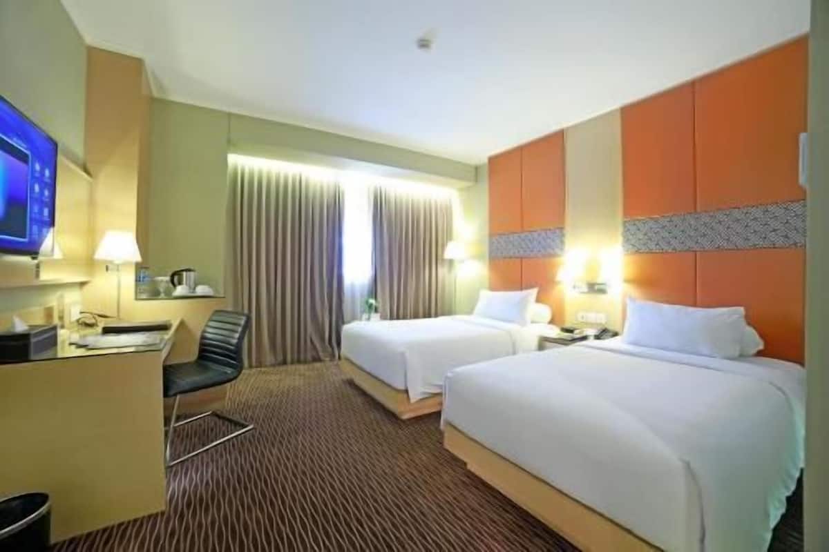 Ein Hotelzimmer mit zwei Betten, einem Schreibtisch, einem Stuhl, einem Fernseher und einem fenster mit Vorhängen.