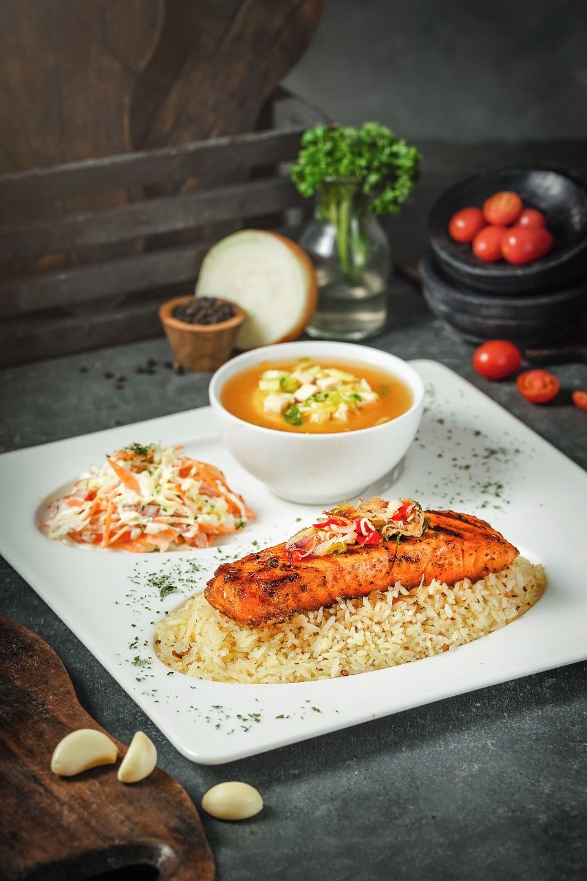 A plate with grilled salmon, rice, and a side of coleslaw.