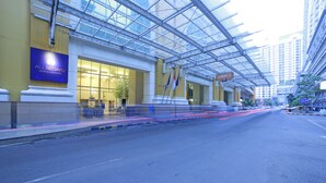 A hotel entrance with a glass facade, a sign for 'All Sedayu Hotels & Resorts', and flags.
