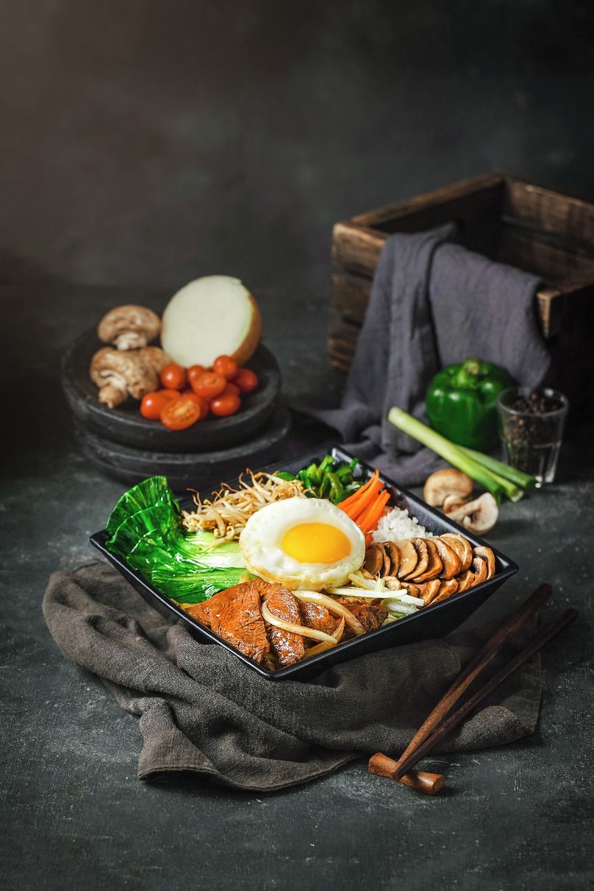 Un plato negro con verduras, fideos y un huevo frito.