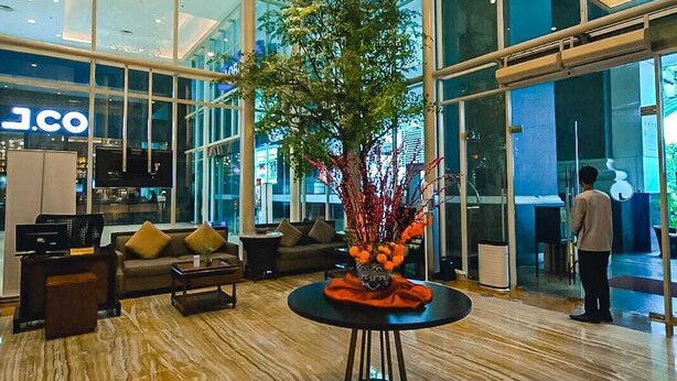 A spacious lobby with a large chandelier, a reception desk, and a seating area with a decorative plant centerpiece.