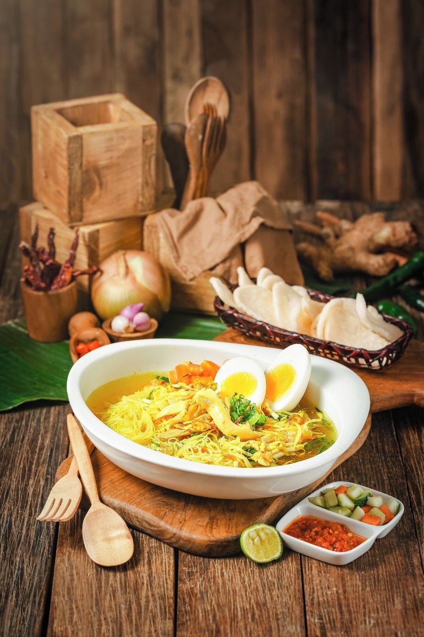Un tazón de sopa de fideos con verduras y un huevo cocido sobre una mesa de madera.