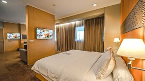 A hotel room with a large bed, a TV mounted on the wall, a desk, and a window with curtains.