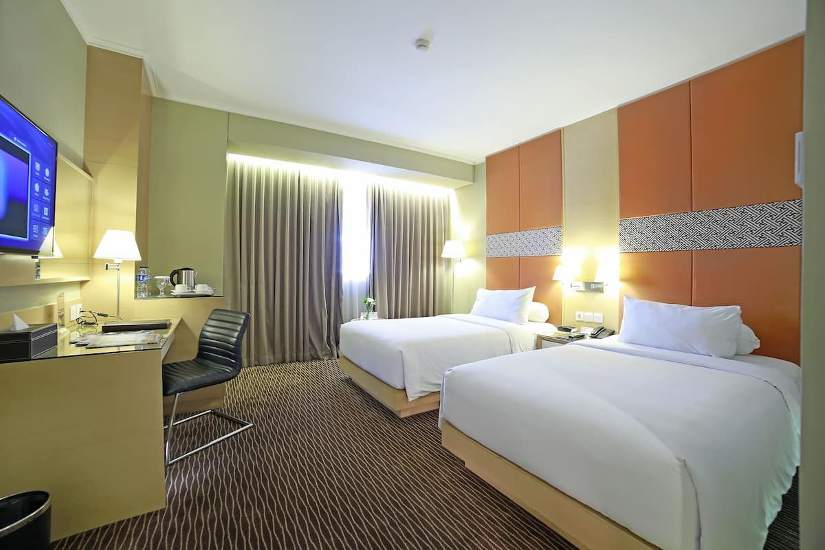 Ein Hotelzimmer mit zwei Betten, einem Schreibtisch, einem Fernseher und einem Badezimmer.