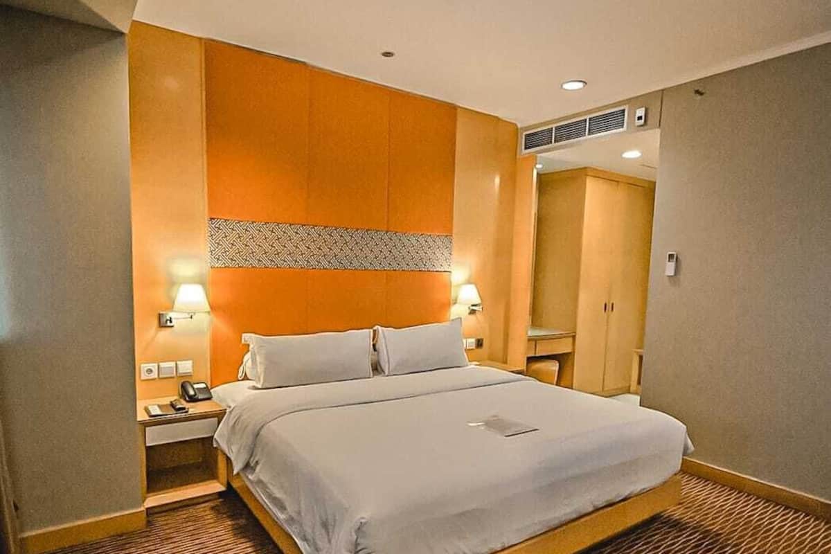Ein Hotelzimmer mit Bett, Nachttischen, einer Lampe, einem Schrank und einer Tür.