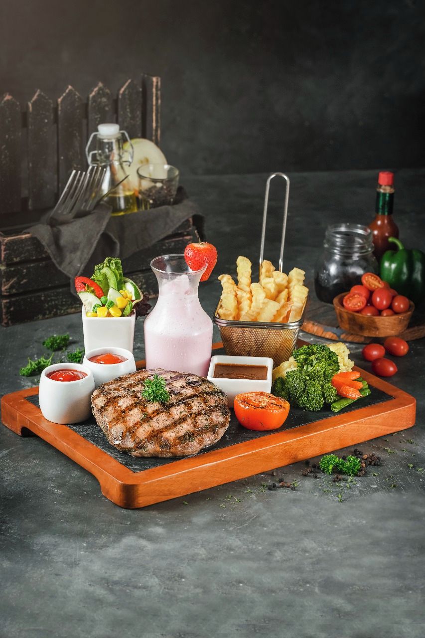A wooden tray with a grilled meat, salad, and drinks.