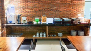 A kitchen area with a brick wall, a coffee machine, a water dispenser, and various kitchen utensils. - Amaliun Hotel (Medan)