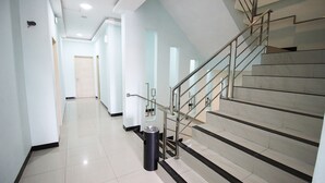 A modern hotel hallway with a staircase, a trash bin, and a door at the end. - Amaliun Hotel (Medan)