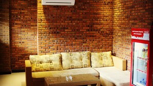 A room with a brick wall, a sofa, a coffee table, and a Coca-Cola refrigerator. - Amaliun Hotel (Medan)