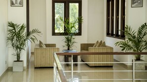 Een moderne woonkamer met een zithoek, een salontafel en twee potplanten. Er is een groot raam met uitzicht op groen.