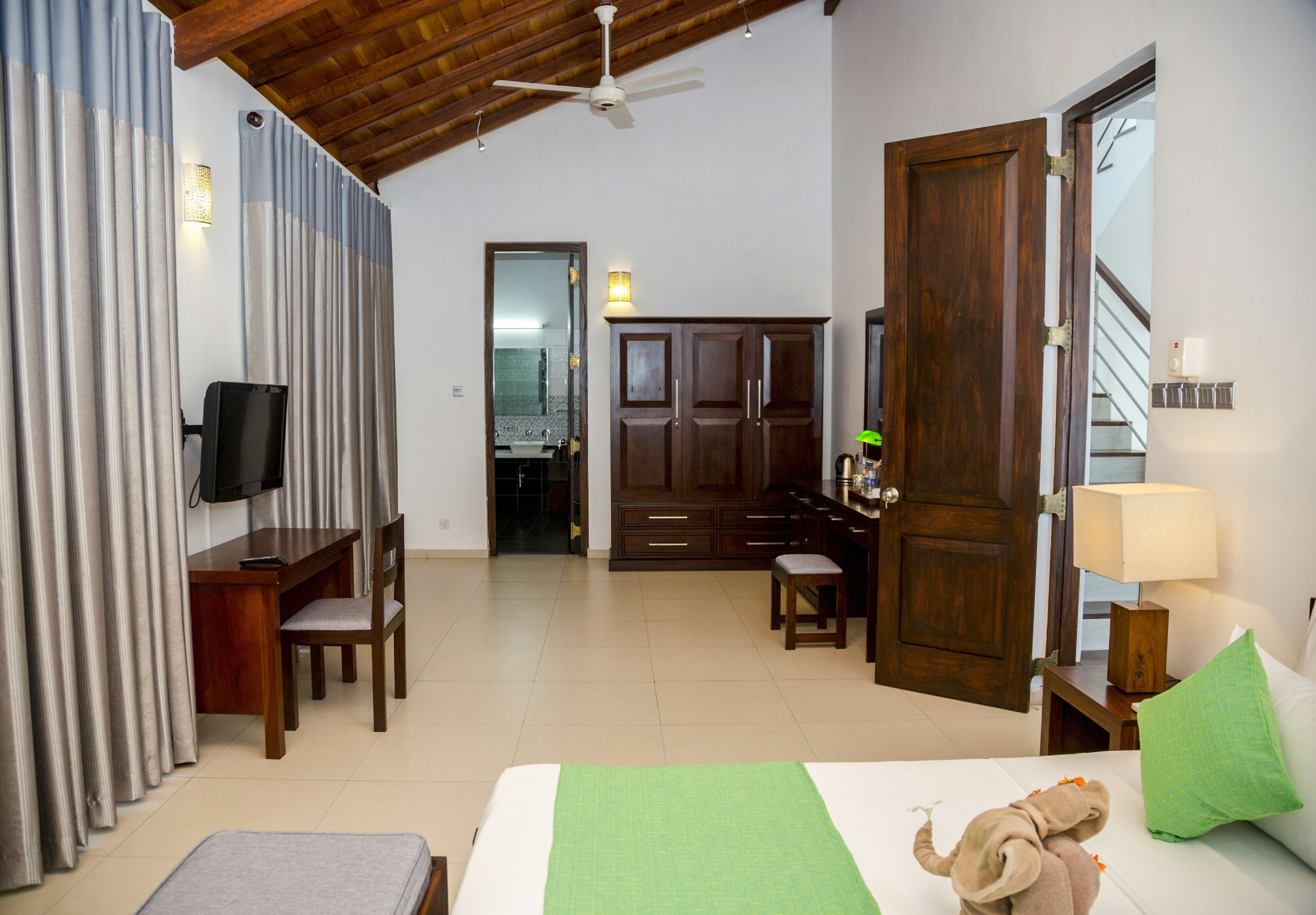 A hotel room with a bed, a desk, a chair, a television, and a wardrobe.
