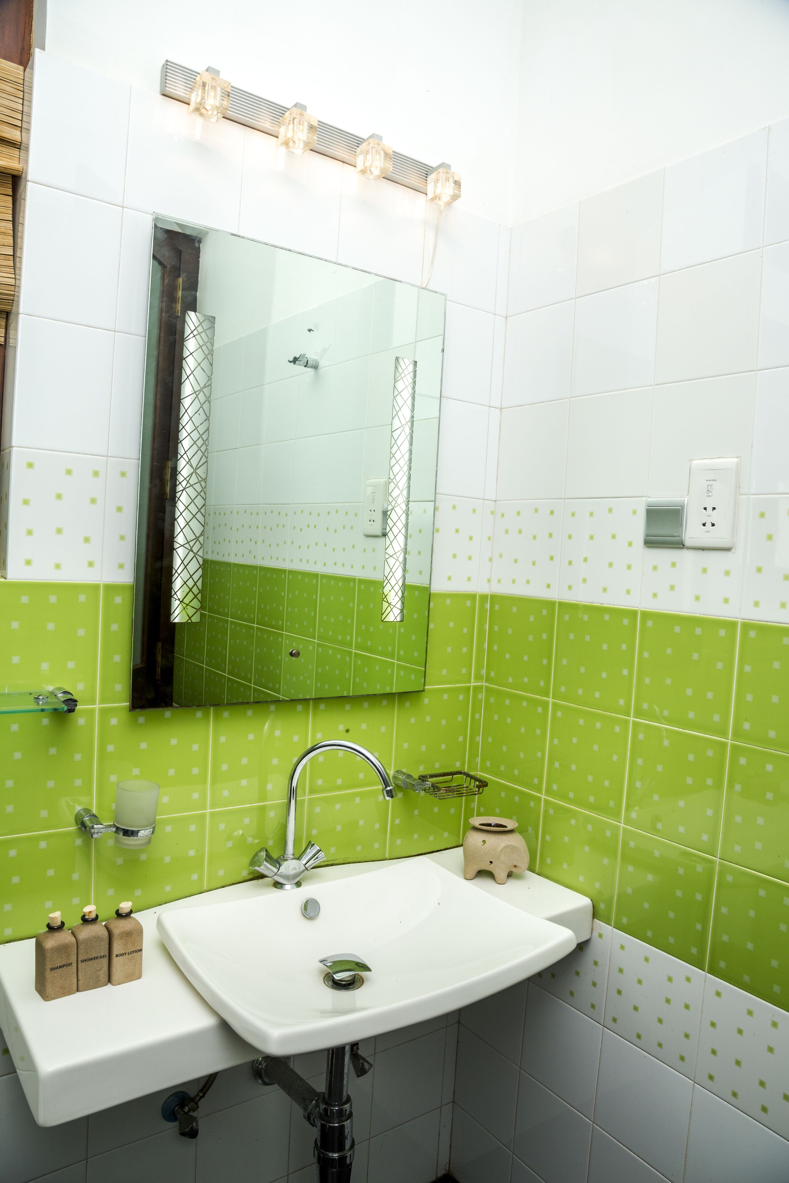 A bathroom with a white sink, green tiled walls, a mirror, and a light fixture above the mirror.