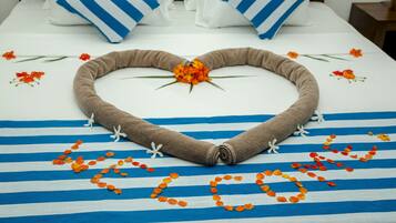 A bed with a heart-shaped towel arrangement, orange petals, and a central flower on a striped bedspread.