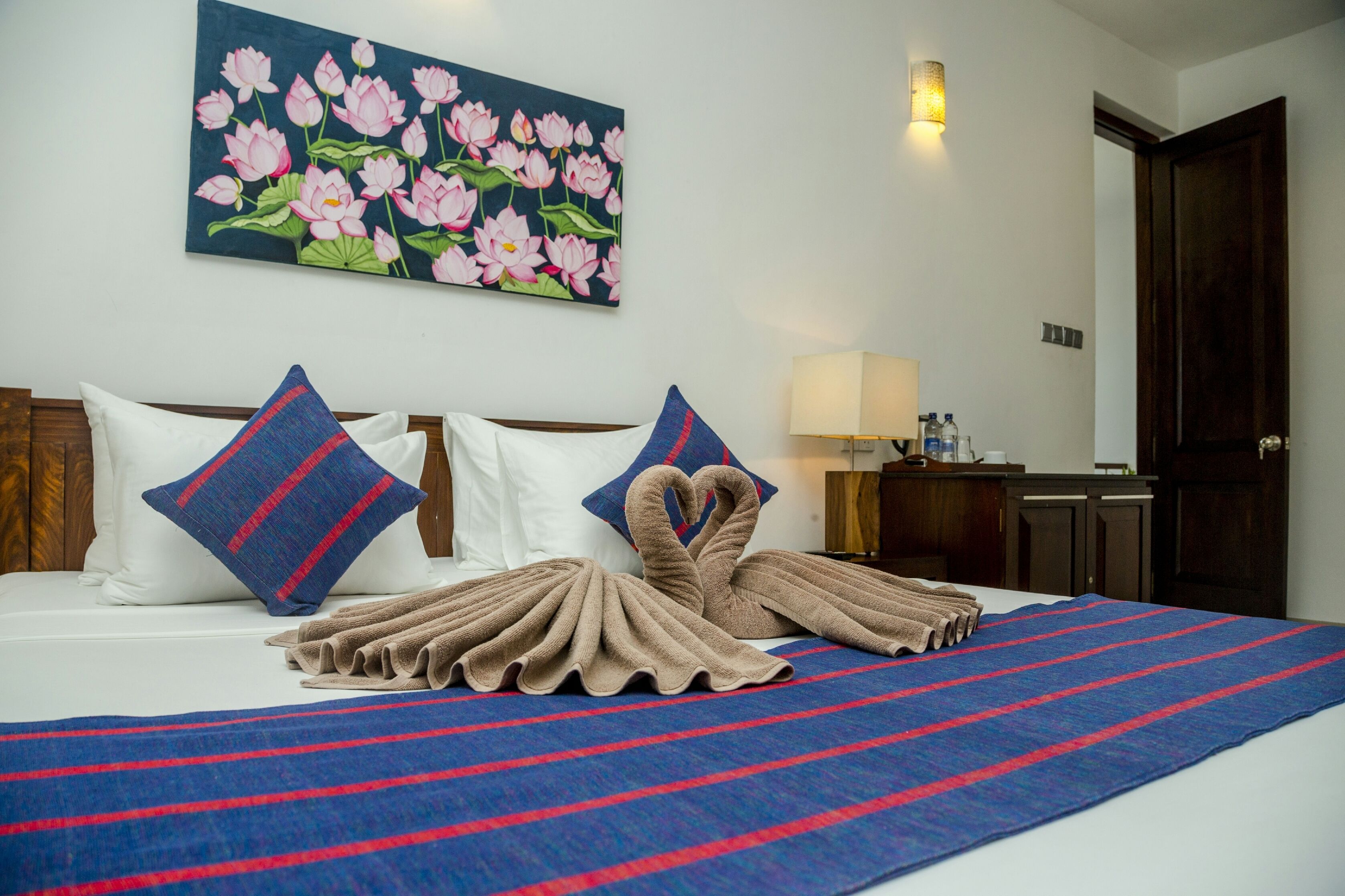 A hotel room with a bed, pillows, a blanket, a painting of flowers, and a lamp.