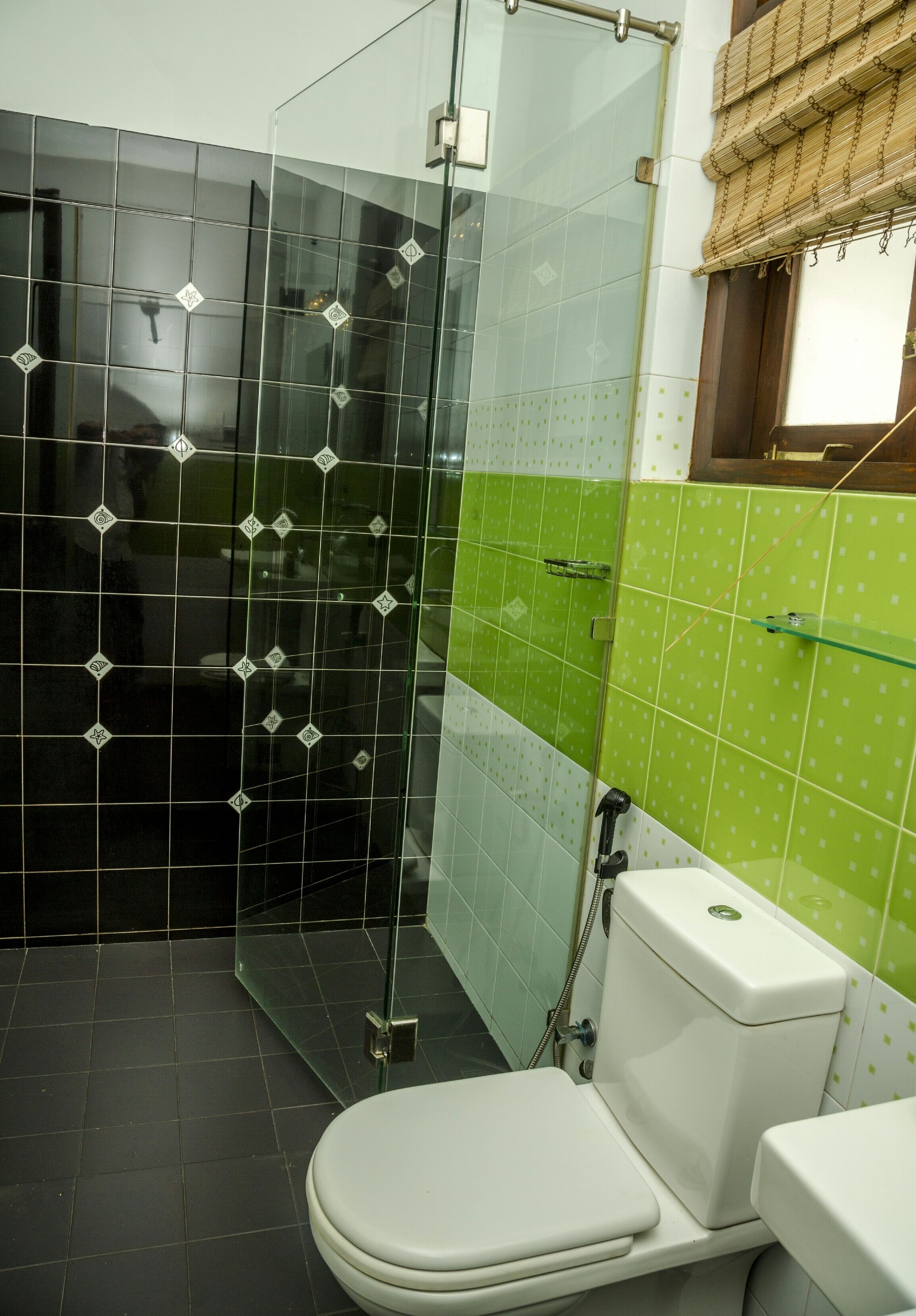 A bathroom with a glass shower enclosure, a toilet, and green tiled walls.