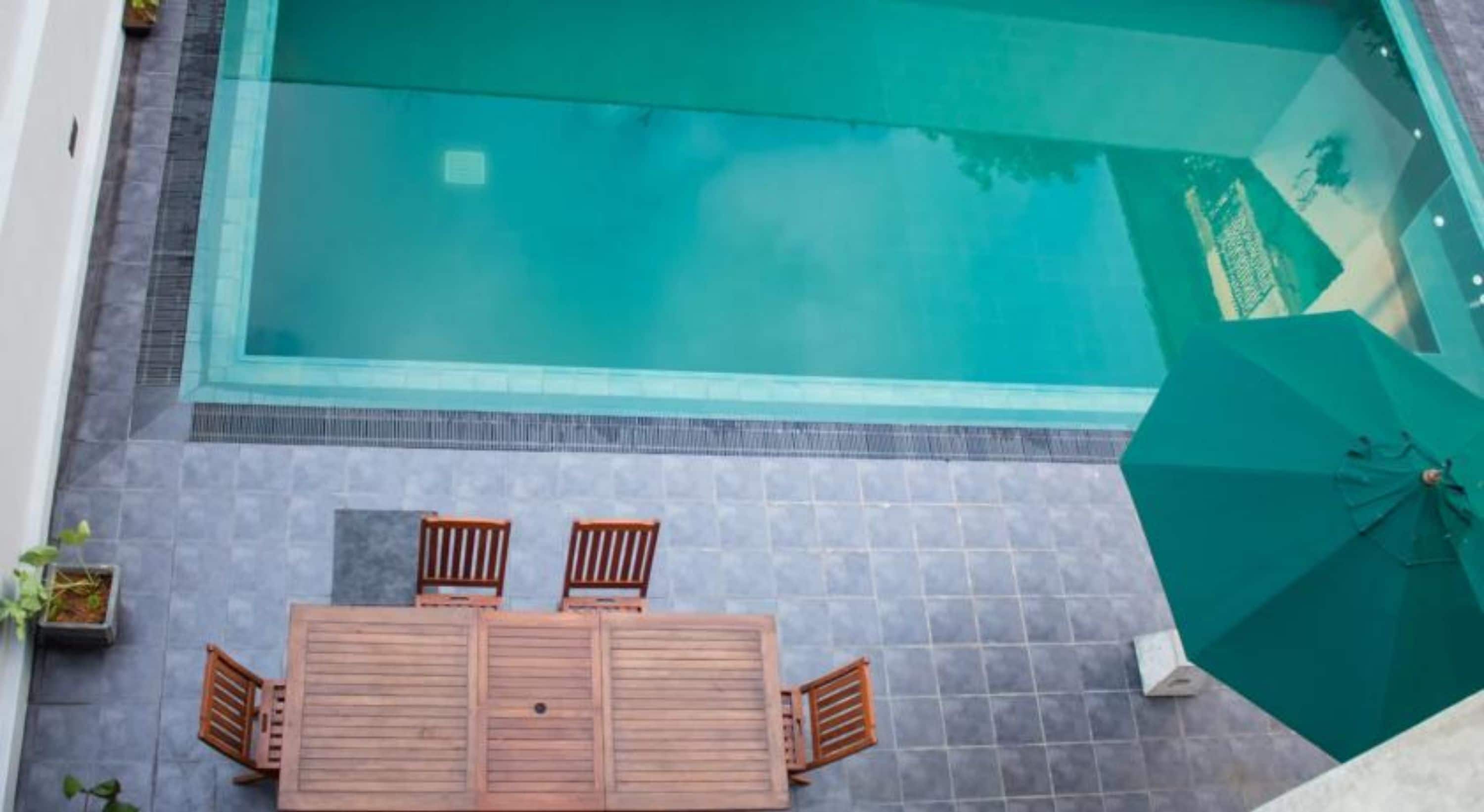 A rooftop pool with a wooden table and chairs, surrounded by a tiled patio.