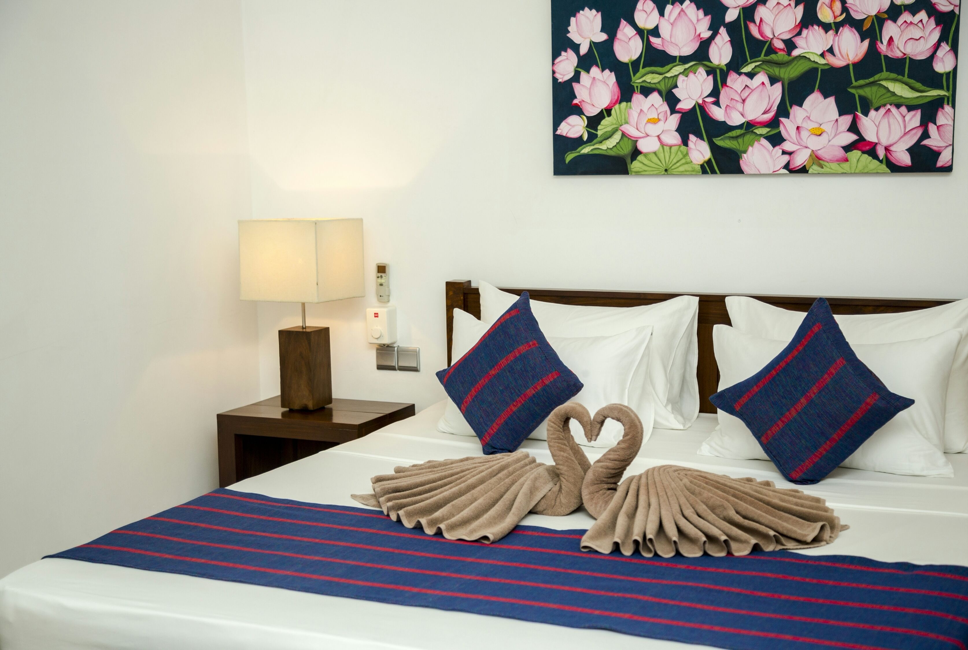 A hotel room with a neatly made bed, a nightstand with a lamp, and a wall painting of pink flowers.