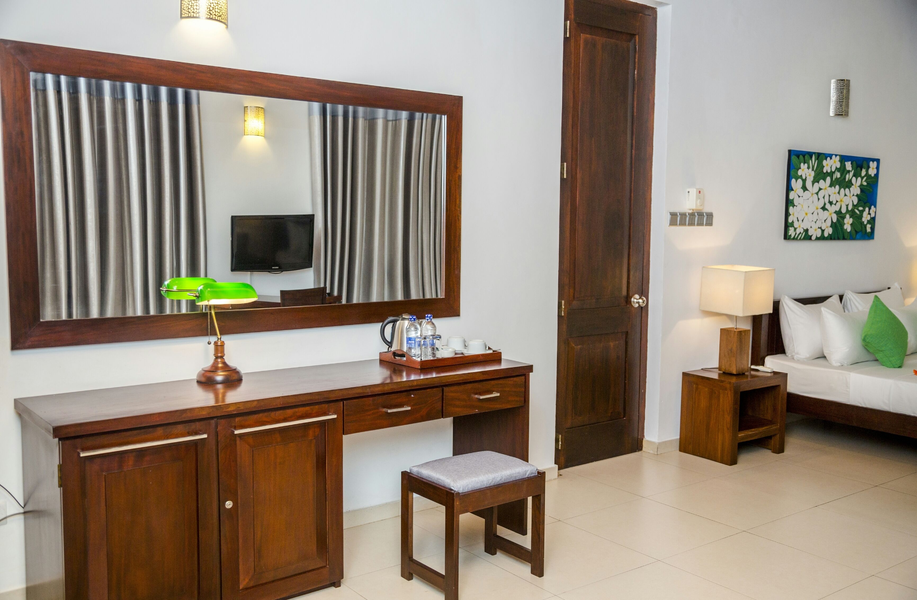 Ein Hotelzimmer mit einem Holztisch, einem Fernseher, einem großen Spiegel, einem Sofa und einem kleinen Tisch mit einer Lampe.