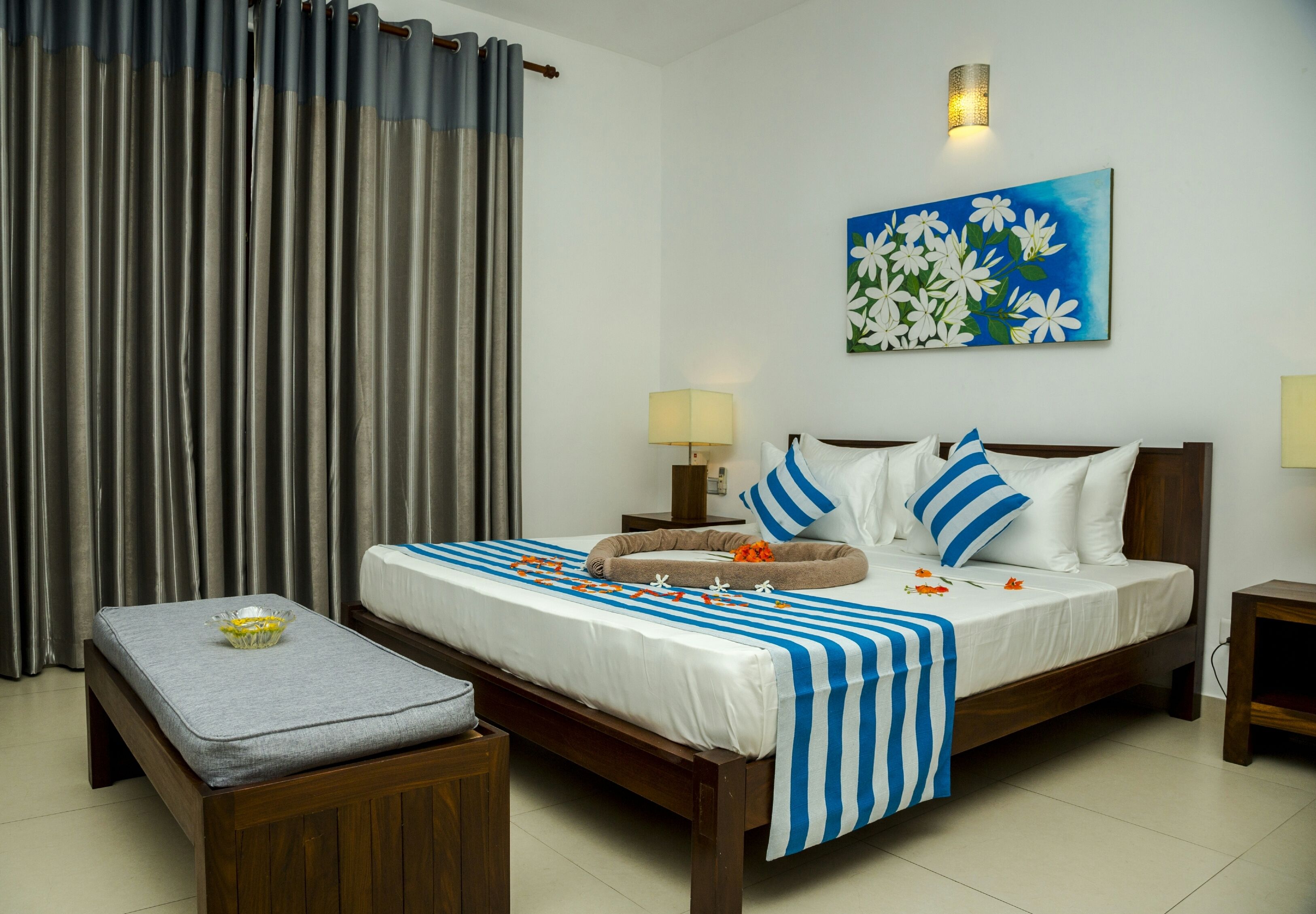 Habitación de hotel ordenada con una cama, mesitas de noche, un banco y un cuadro en la pared.