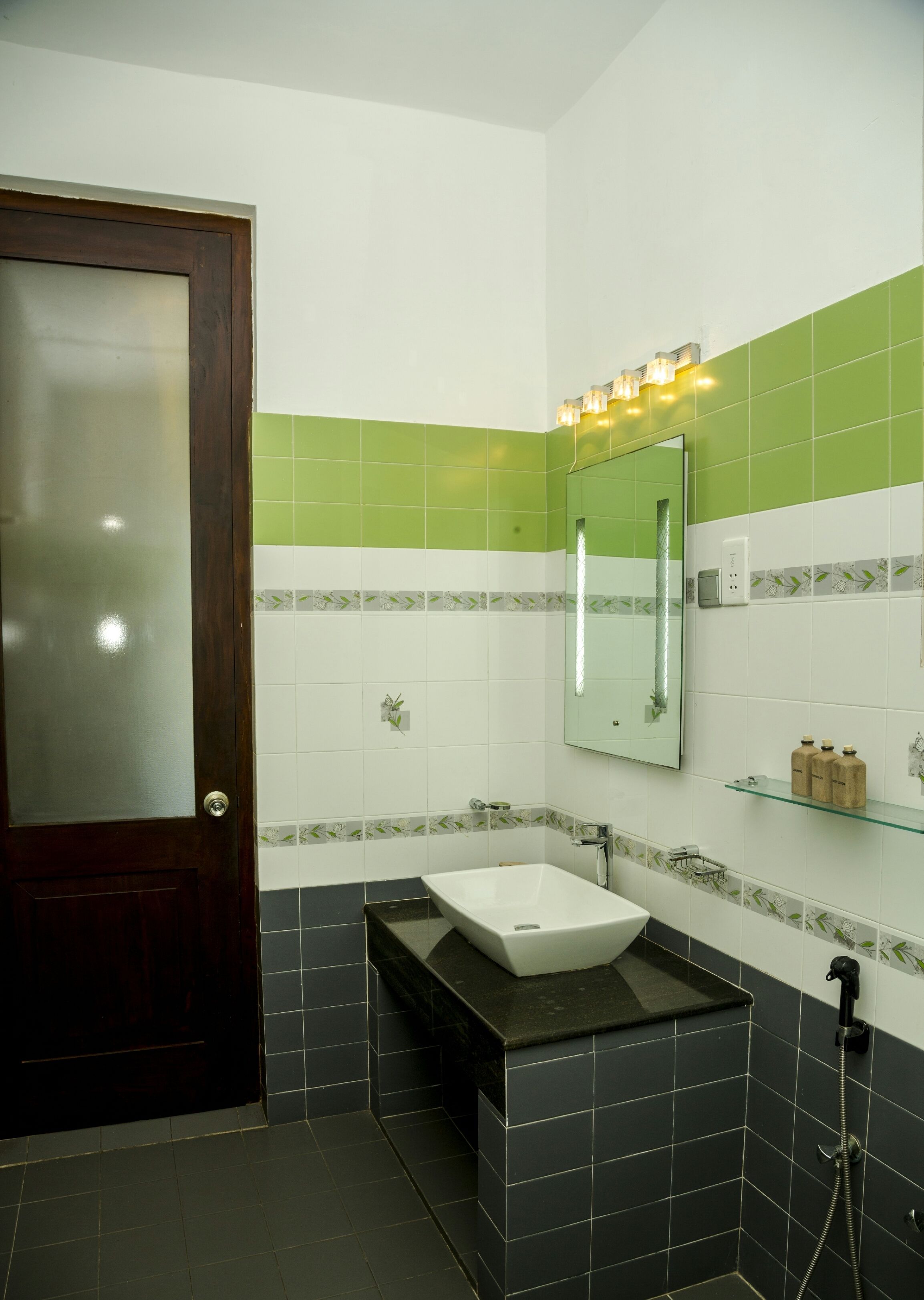 A bathroom with a dark wooden door, a white sink with a black countertop, and green and white tiled walls.