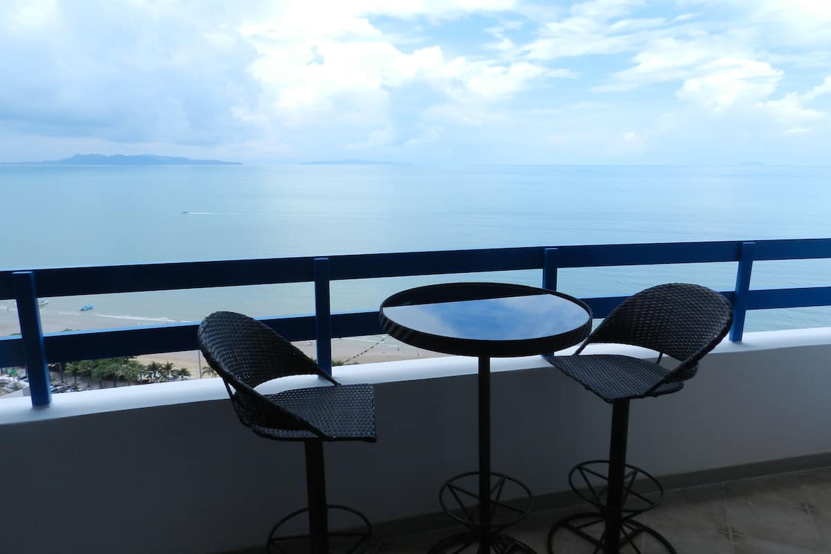 A balcony with two chairs and a small table, overlooking a beach and the sea.