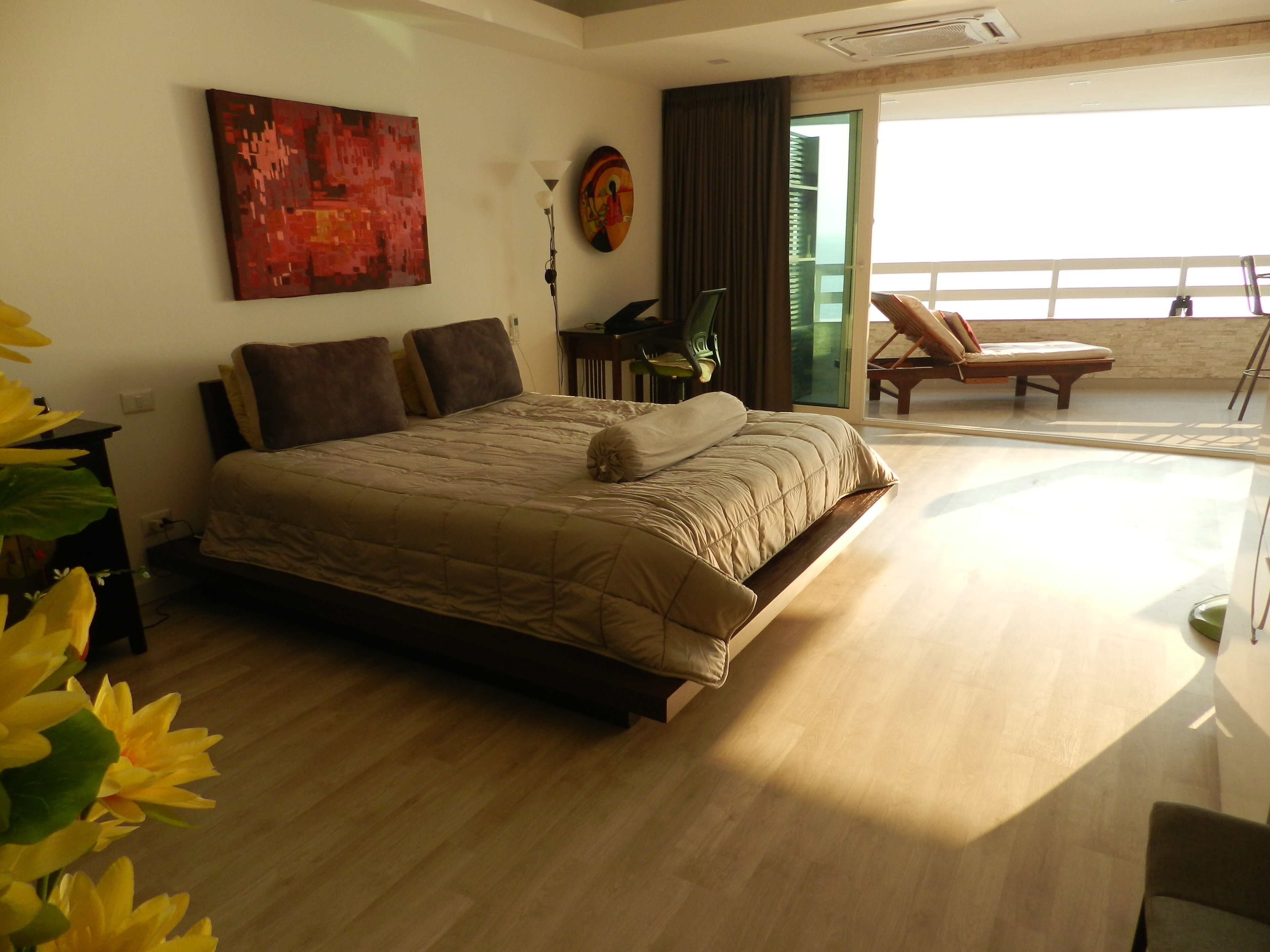 Ein Schlafzimmer mit einem großen Bett, einem Schreibtisch und einem Stuhl. Es gibt einen Balkon mit einem Stuhl und einem Tisch.