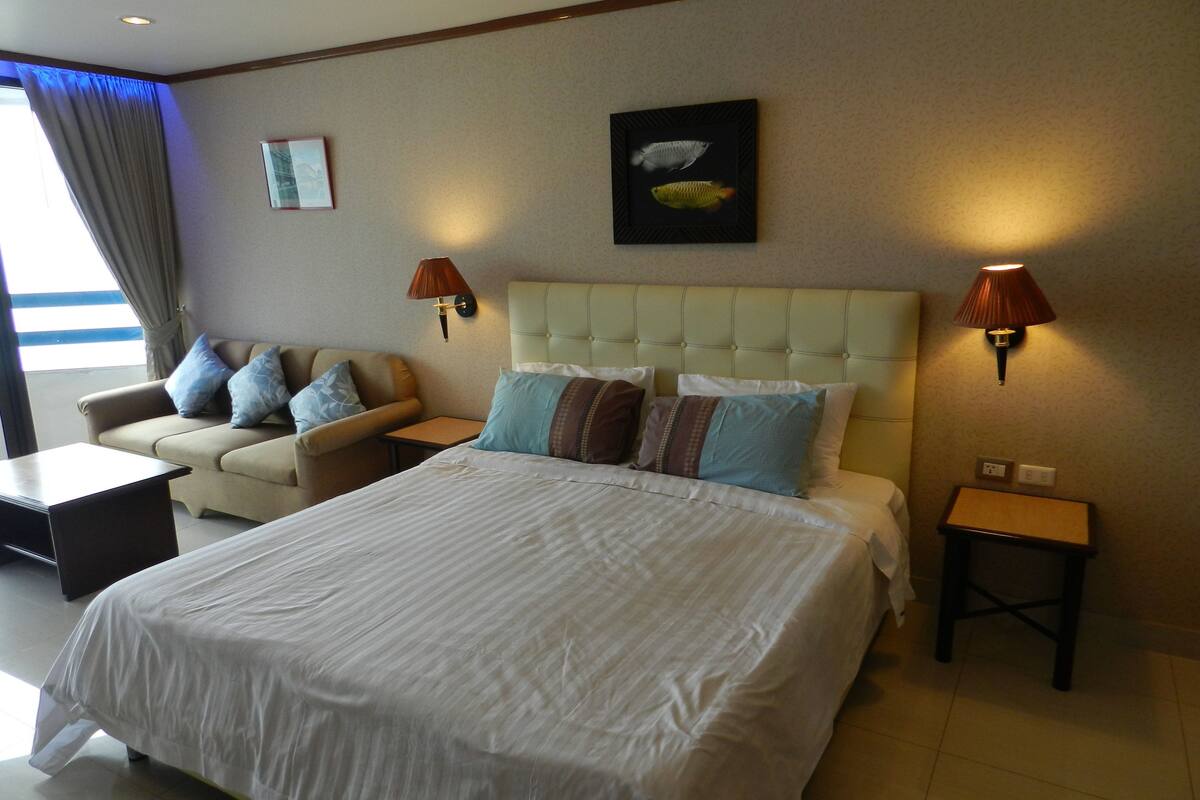 A hotel room with a large bed, a sofa, two wall-mounted lamps, and a framed picture on the wall.