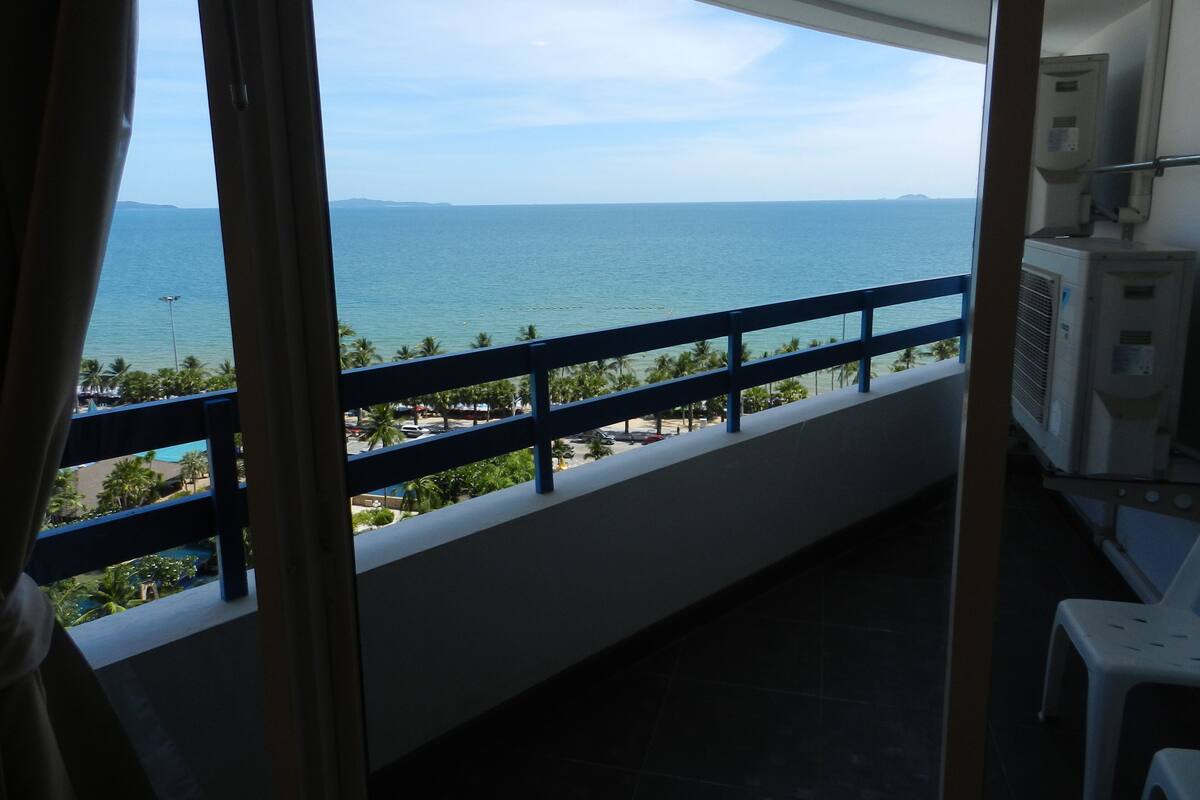 A balcony with a view of the sea, a railing, and a white chair.