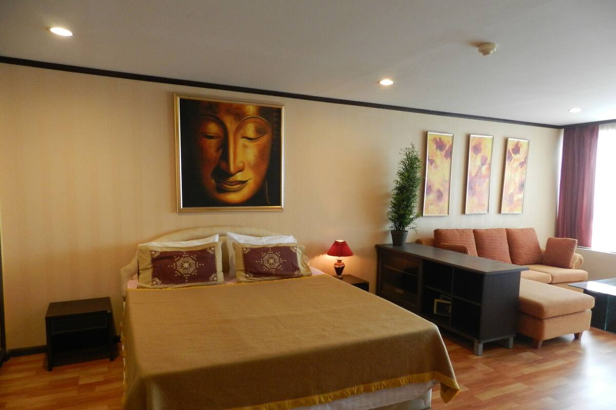 A hotel room with a bed, a sofa, a desk, and a large Buddha painting on the wall.