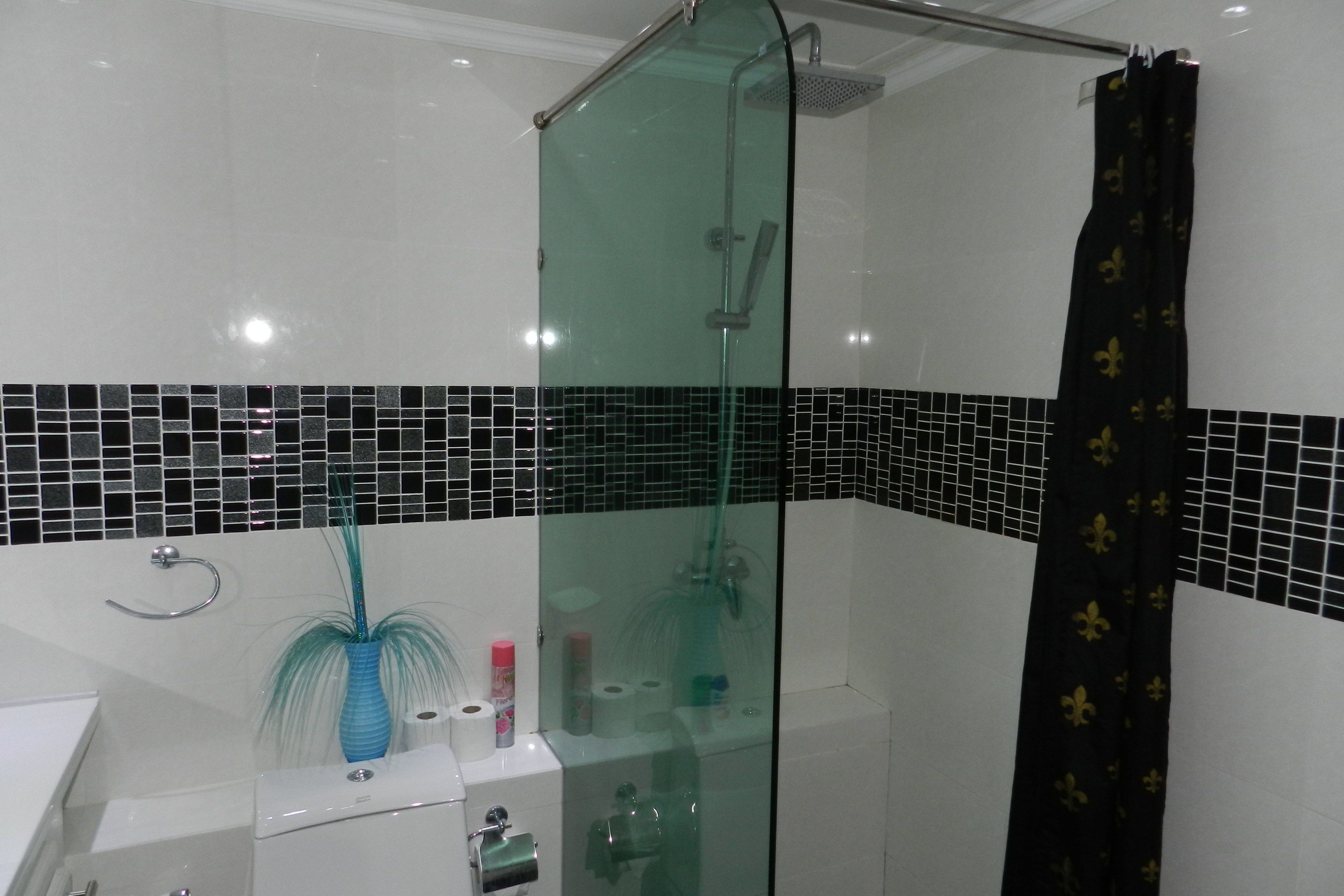 A modern bathroom with a glass-enclosed shower, a white sink, and a black and white tiled backsplash.
