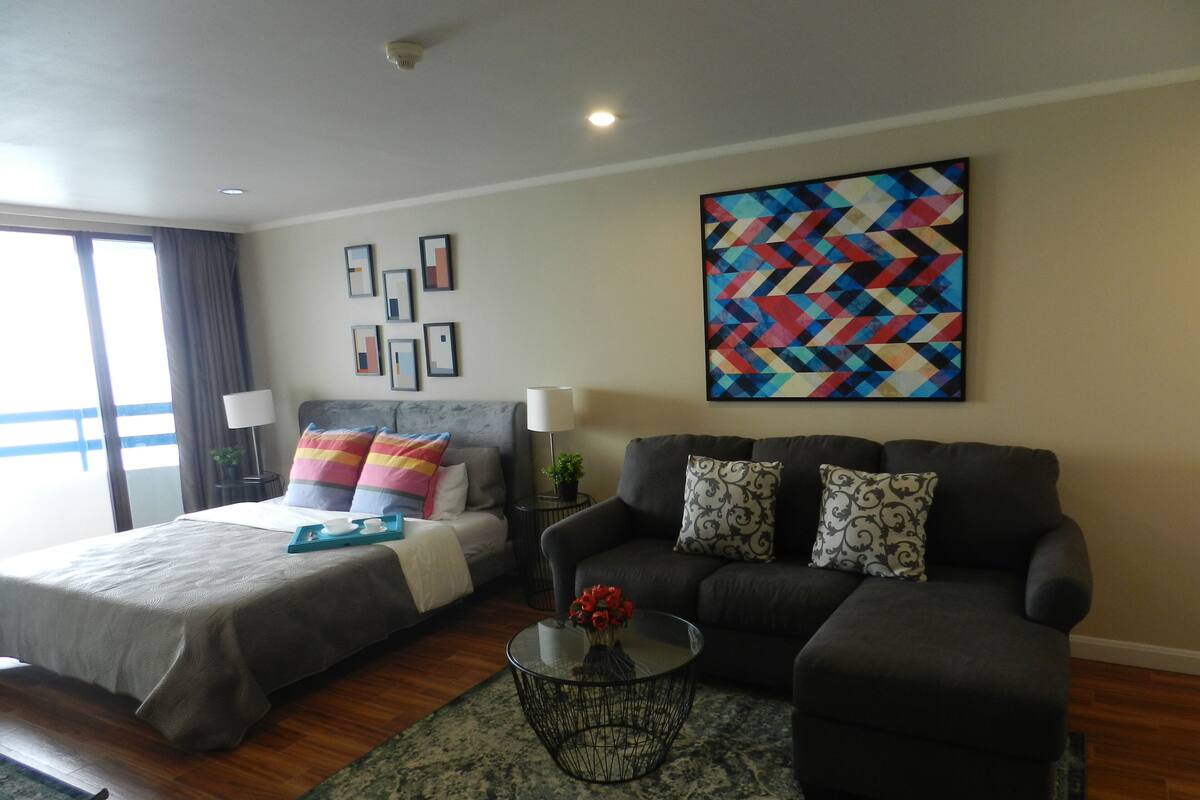 A modern hotel room with a bed, a sofa, a coffee table, and a large abstract painting on the wall.
