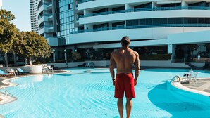 Un hombre de pie al borde de una piscina, con un edificio moderno de fondo.