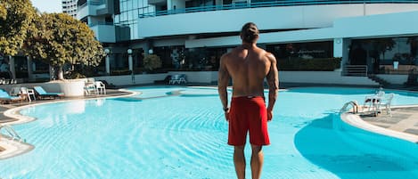 En man står vid kanten av en swimmingpool, med en modern byggnad i bakgrunden.