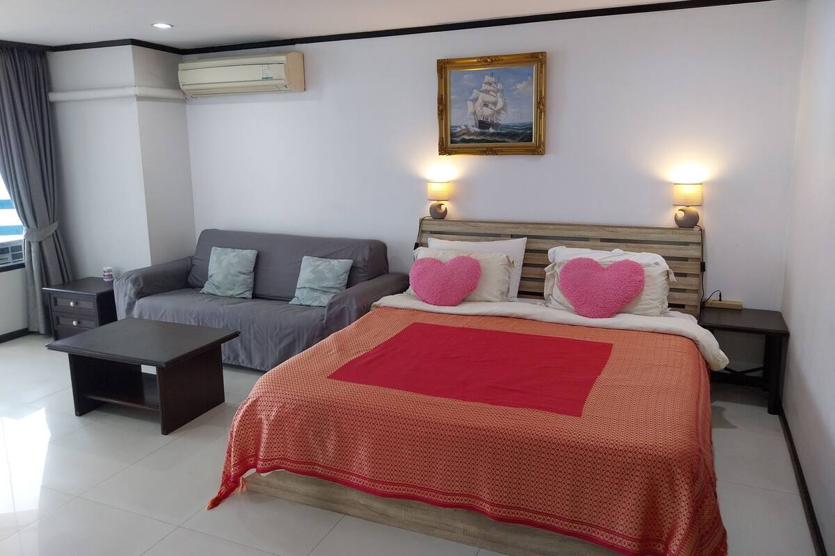 A bedroom with a bed, a sofa, a nightstand, and a wall-mounted air conditioner.