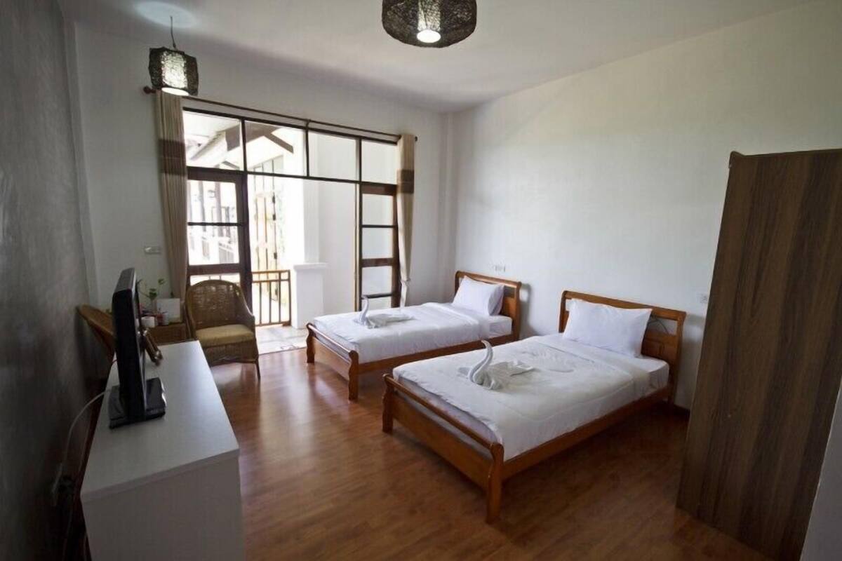 A hotel room with two wooden beds, a desk with a computer, a chair, and a large window with curtains.
