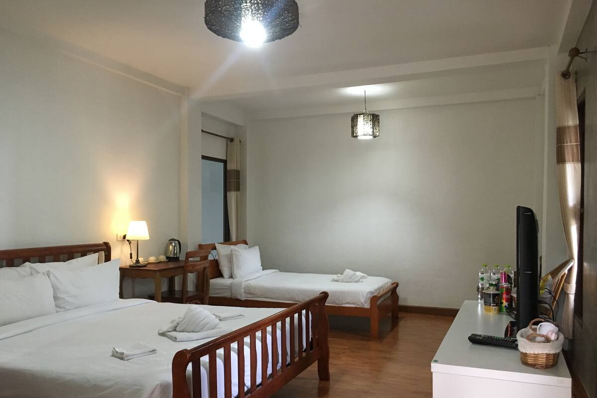 A hotel room with two single beds, a desk with a television, and a small table with a lamp.