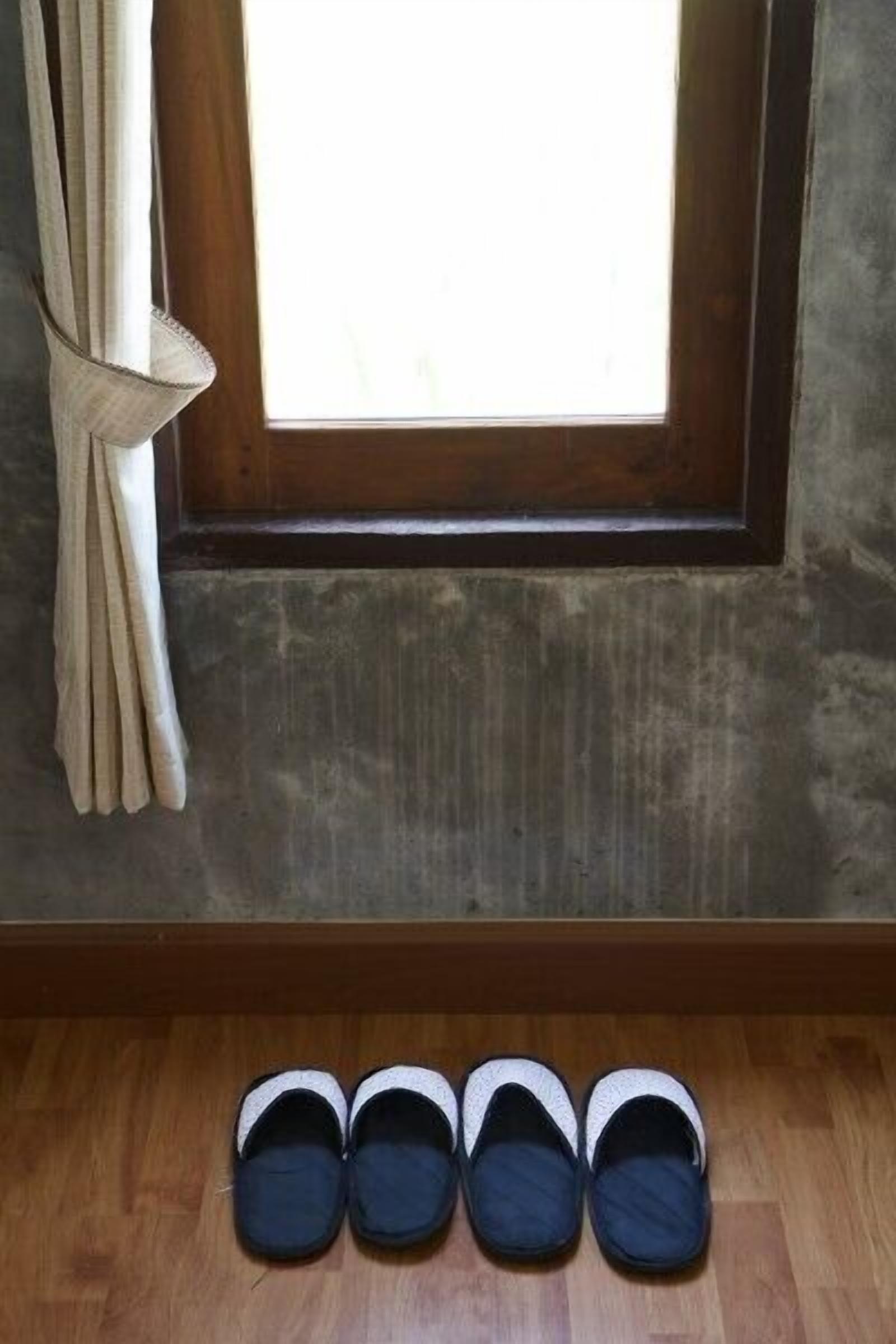 A window with curtains, a wooden floor, and a pair of slippers.