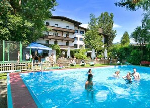 A swimming pool with people in it, surrounded by a fence, and a building in the background. - Hotel Linde (Woergl)