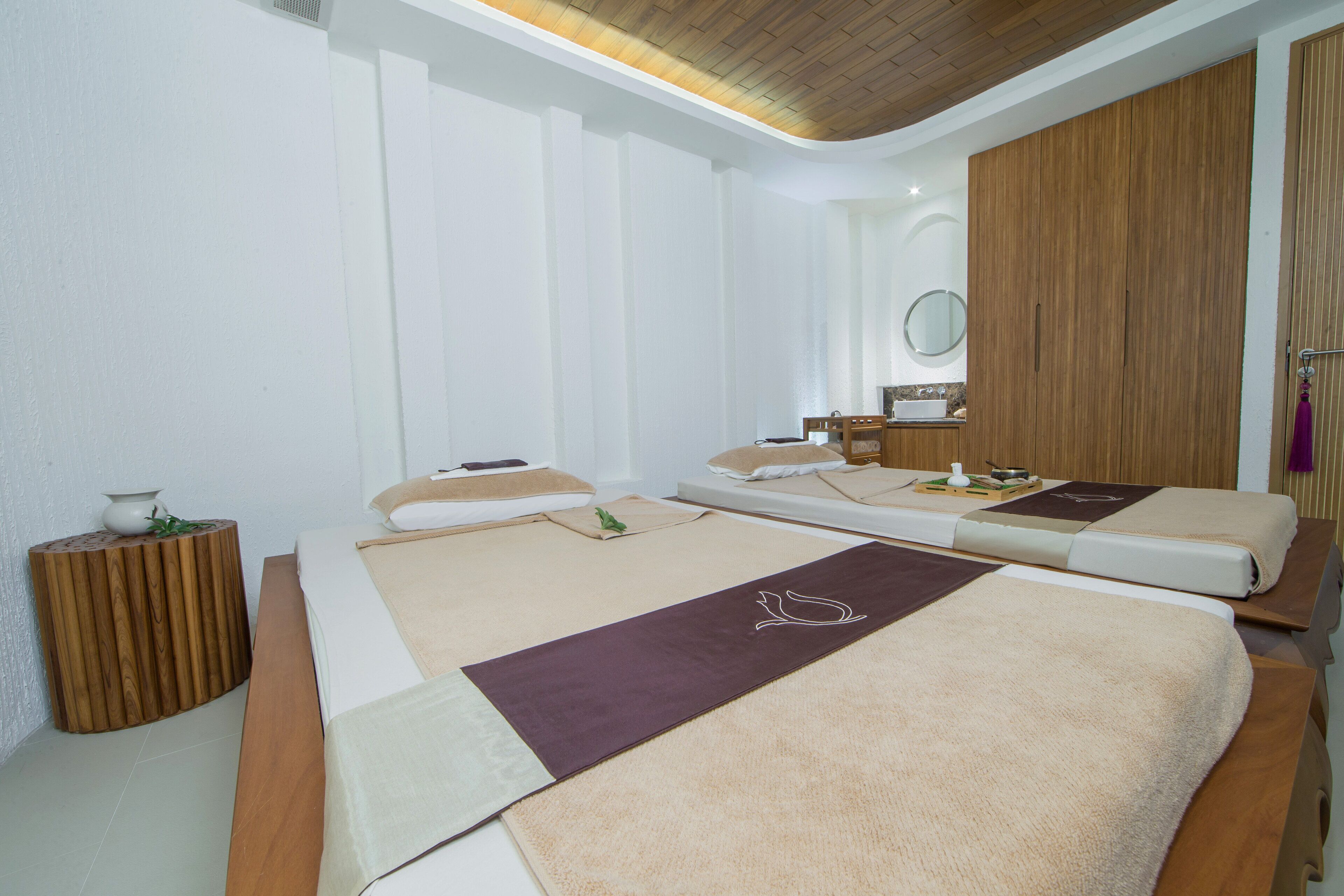 A spa room with two beds, a wooden side table, a mirror, and a wooden wardrobe.