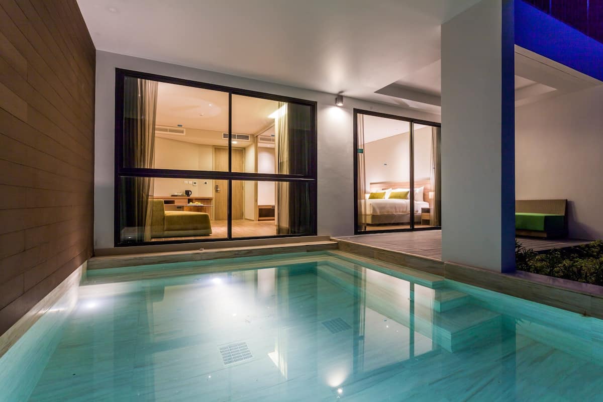 A modern hotel room with a large glass door leading to a balcony, a pool, and a well-lit interior.