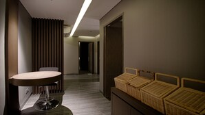 Una habitación de hotel moderna con una mesa redonda, una silla, un pequeño sofá y una mesita de mimbre.