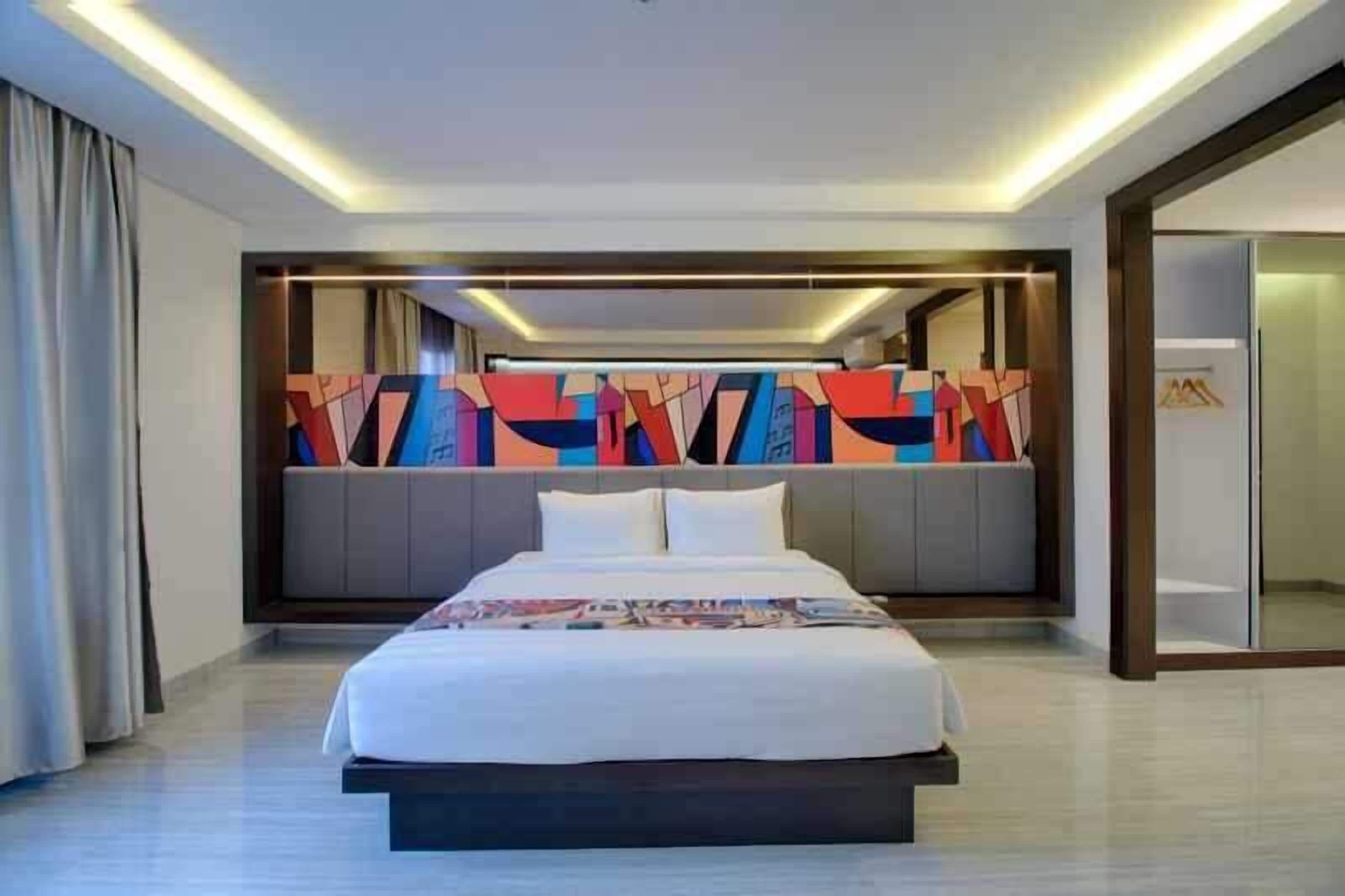 Une chambre d’hôtel moderne dotée d’un grand lit, d’une œuvre d’art abstraite aux couleurs vives au niveau de la tête de lit, et d’un design élégant et contemporain.