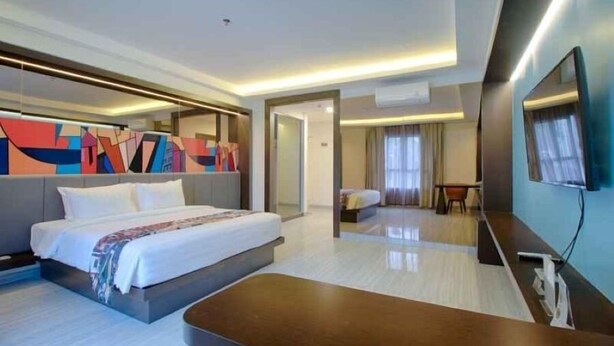 Habitación de hotel moderna con una cama grande, un escritorio, un televisor y un colorido cuadro abstracto en la pared.
