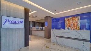 Zona de recepción de un hotel con un mostrador de mármol, una gran obra de arte de Picasso y un cartel del hotel Picasso.